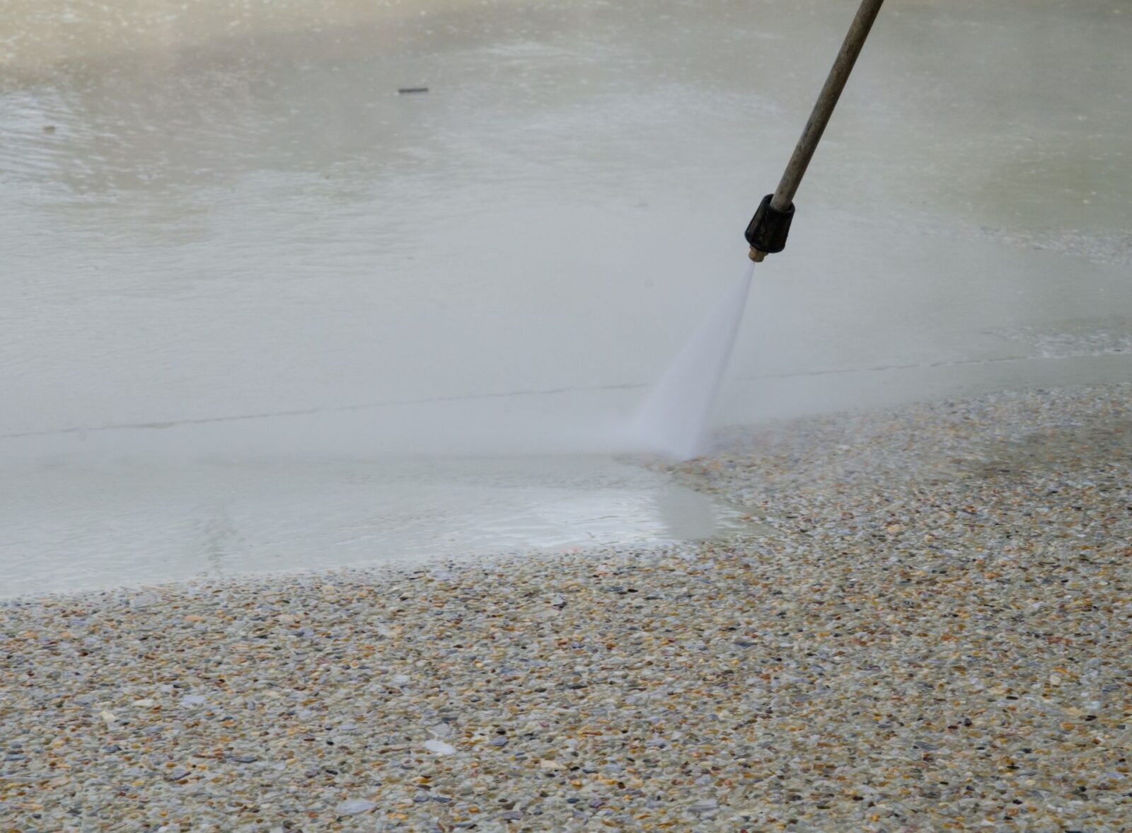 A power washer is being used by a concrete contractor in Gilbert AZ to clean a concrete surface. The high-pressure water stream is visibly effective, removing dirt and grime as it travels across the area. The image captures the contrast between the cleaned section and the still-dirty part of the concrete.