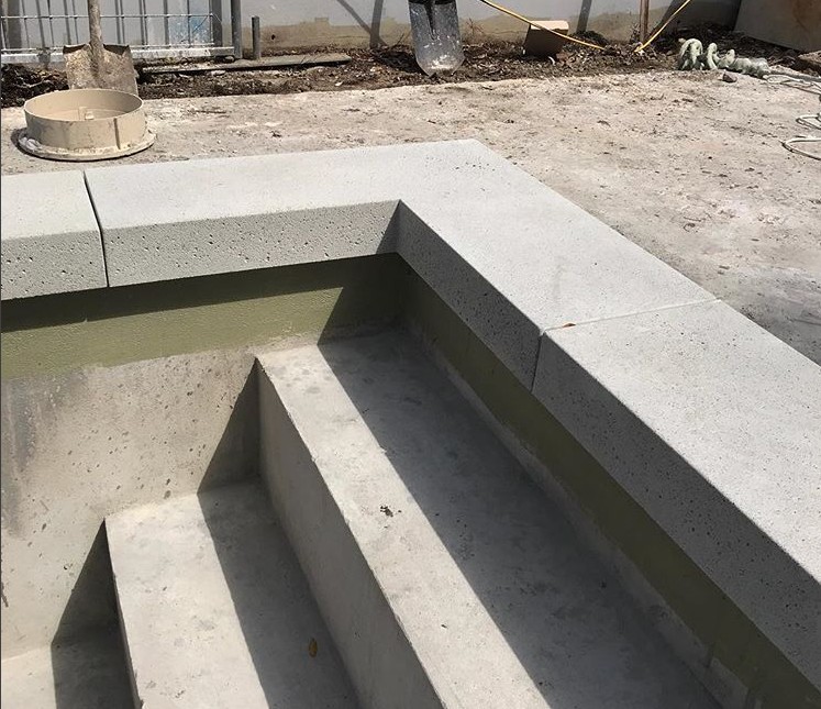 Concrete steps leading into an unfinished swimming pool with a partially built retaining wall along the edge. Construction materials and debris are scattered around the area, awaiting the skilled touch of East Valley Concrete, a top concrete contractor in Chandler AZ.